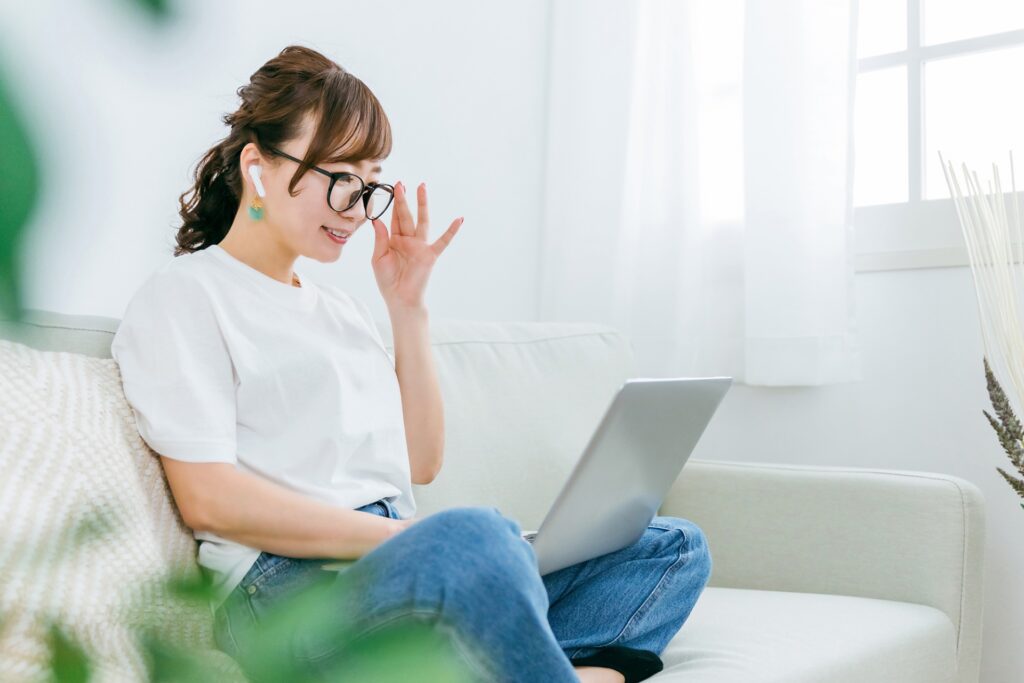 イヤホンとメガネをつけている女性がパソコンを使っている