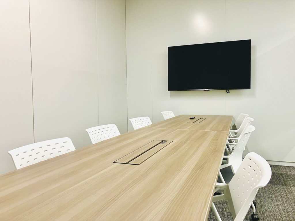 白い椅子と長テーブル、モニターのある会議室
