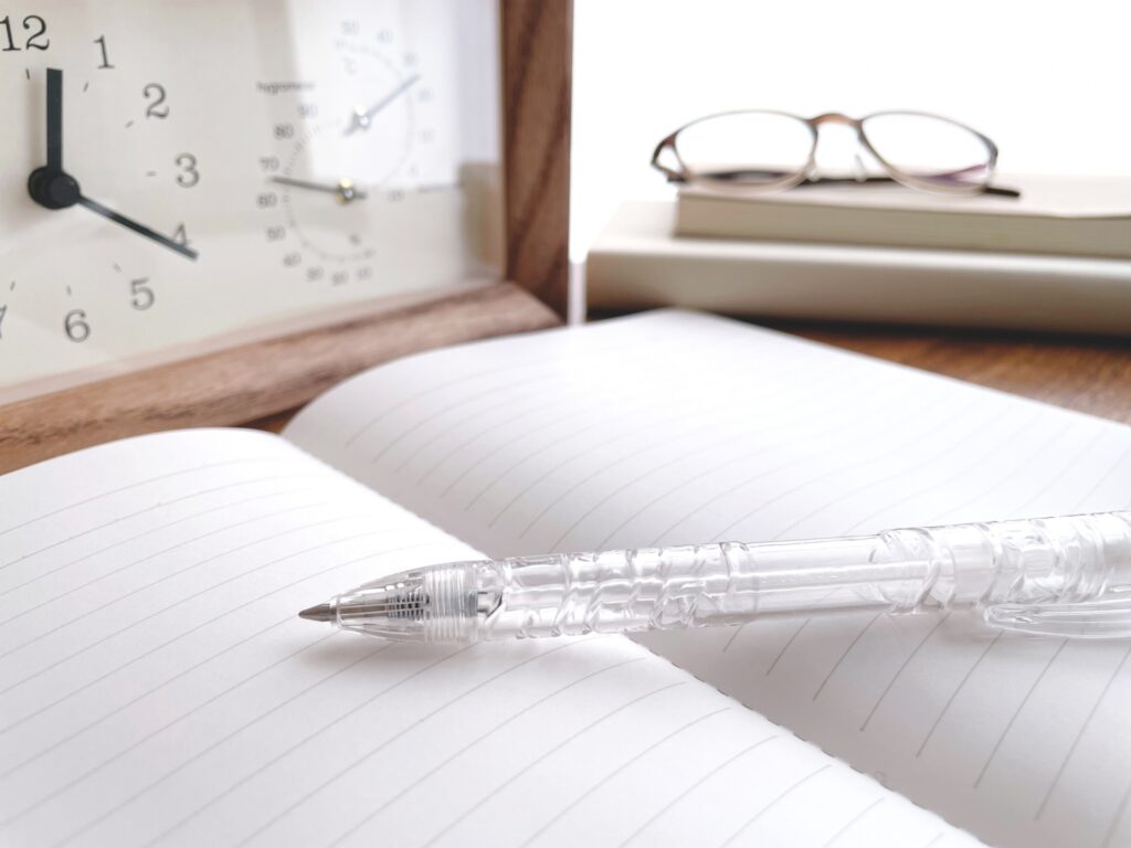 時計の前にあるノートと透明のペン