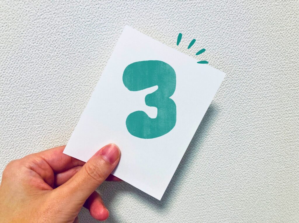 緑の３が描かれているカードを持っている女性の手